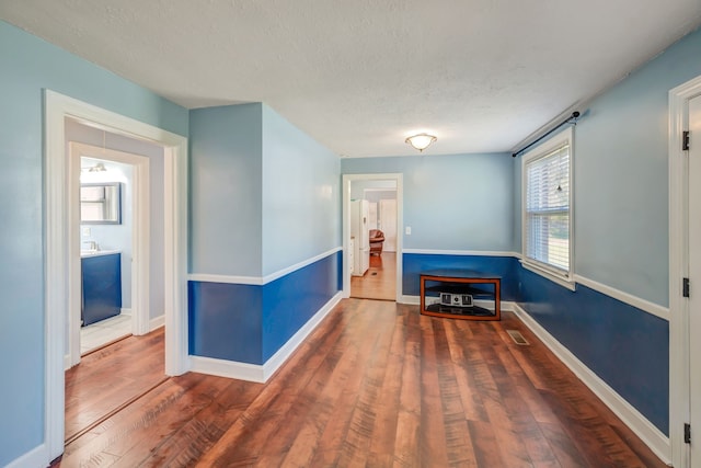 corridor with a textured ceiling and dark wood-type flooring