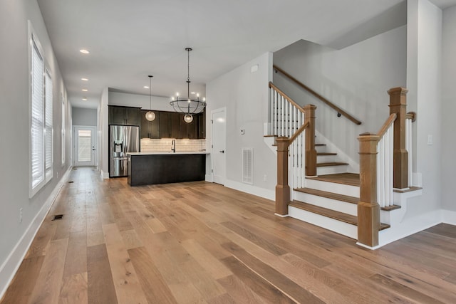 unfurnished living room featuring an inviting chandelier, light hardwood / wood-style flooring, and sink