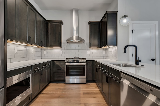 kitchen with tasteful backsplash, stainless steel appliances, light wood-type flooring, decorative light fixtures, and wall chimney range hood