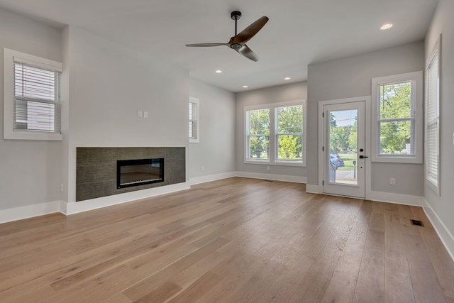 unfurnished living room with ceiling fan, light hardwood / wood-style floors, and a tile fireplace