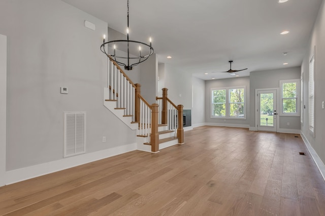 unfurnished living room featuring ceiling fan with notable chandelier and light hardwood / wood-style floors