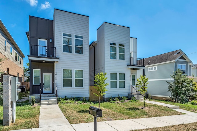 contemporary house with central AC unit, a balcony, and a front lawn