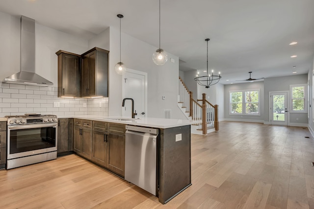 kitchen featuring appliances with stainless steel finishes, light wood-type flooring, decorative light fixtures, sink, and wall chimney range hood