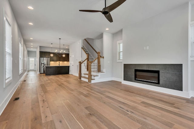 unfurnished living room featuring ceiling fan with notable chandelier, wood-type flooring, and a tiled fireplace