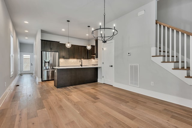 kitchen with hanging light fixtures, dark brown cabinets, light hardwood / wood-style flooring, stainless steel refrigerator with ice dispenser, and decorative backsplash