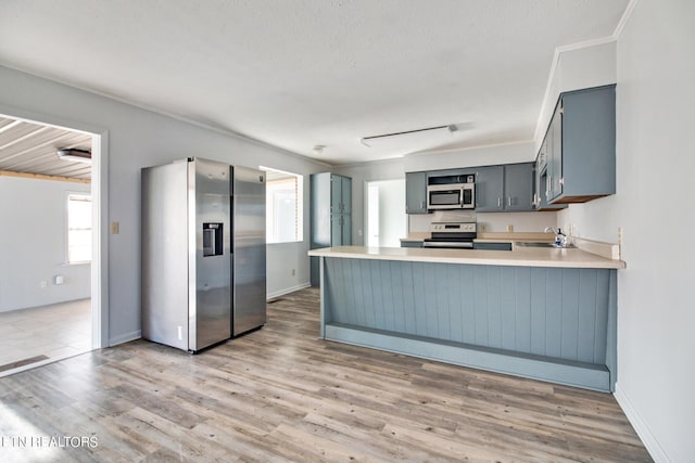 kitchen with a sink, light countertops, a peninsula, stainless steel appliances, and light wood-style flooring