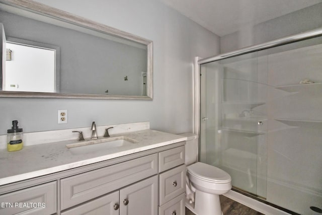 full bathroom with toilet, vanity, a stall shower, and wood finished floors