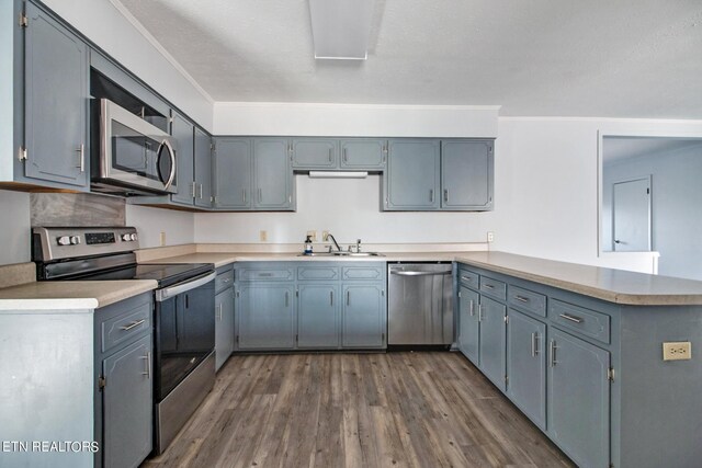 kitchen with appliances with stainless steel finishes, a peninsula, light countertops, dark wood finished floors, and a sink