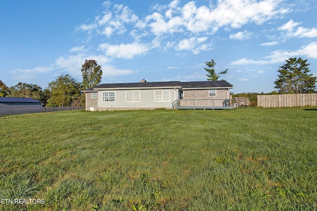 back of property with a wooden deck, fence, and a lawn