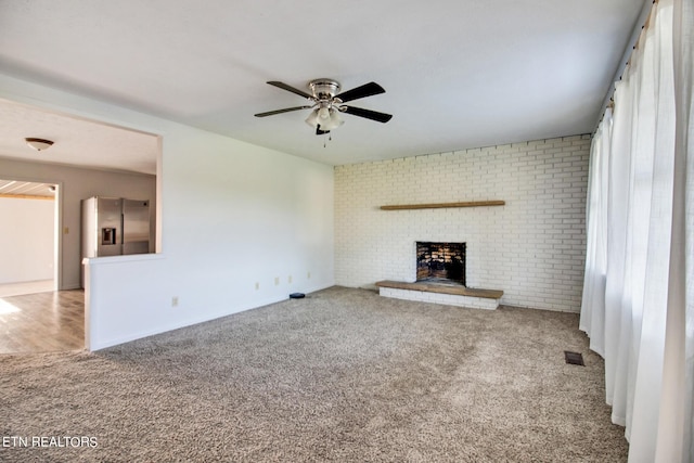 unfurnished living room with carpet, a ceiling fan, visible vents, a brick fireplace, and brick wall