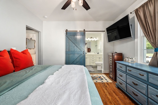 bedroom with ceiling fan, a barn door, connected bathroom, and dark hardwood / wood-style floors