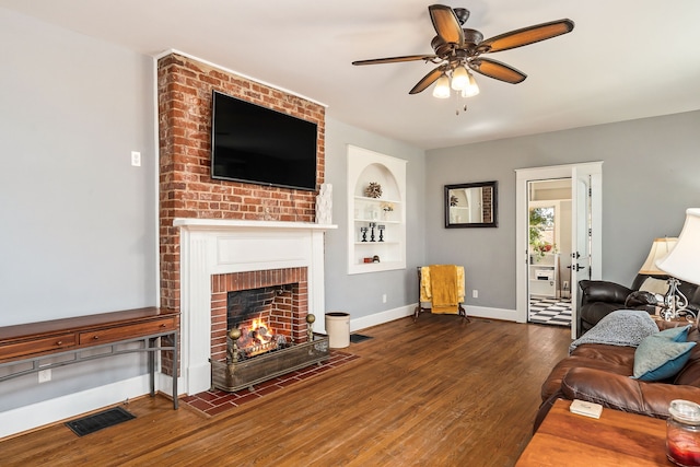 living room with built in features, a fireplace, ceiling fan, and dark wood-type flooring