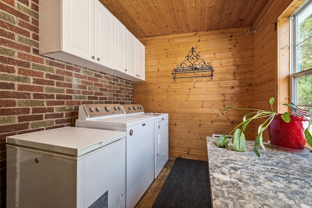 laundry area with wooden walls, separate washer and dryer, brick wall, and cabinets