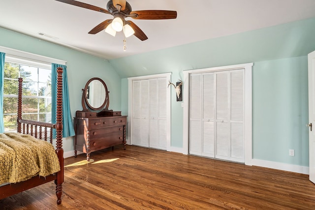 bedroom featuring hardwood / wood-style floors, ceiling fan, vaulted ceiling, and two closets