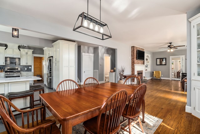 dining area featuring a brick fireplace, dark hardwood / wood-style flooring, and ceiling fan