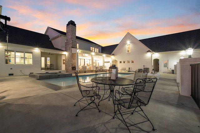 pool at dusk with an in ground hot tub and a patio area