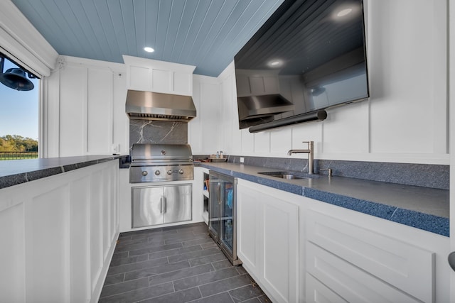 kitchen featuring decorative backsplash, wood ceiling, white cabinets, sink, and wall chimney range hood