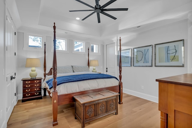 bedroom with light hardwood / wood-style floors, a raised ceiling, and ceiling fan