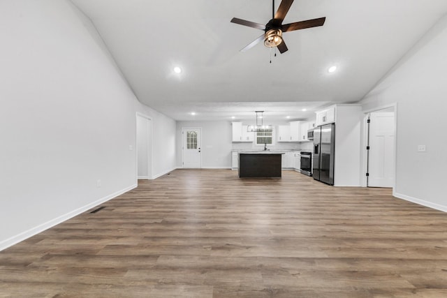 unfurnished living room with lofted ceiling, ceiling fan with notable chandelier, wood finished floors, a sink, and visible vents