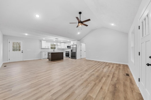 unfurnished living room with light wood-style floors, lofted ceiling, a healthy amount of sunlight, and ceiling fan with notable chandelier