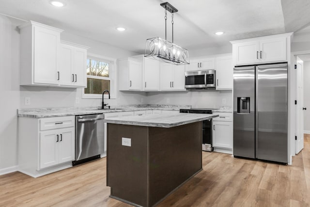 kitchen featuring stainless steel appliances, white cabinets, a sink, a kitchen island, and light wood-type flooring