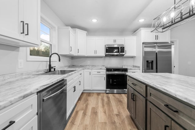 kitchen with light wood-style floors, appliances with stainless steel finishes, white cabinets, and a sink