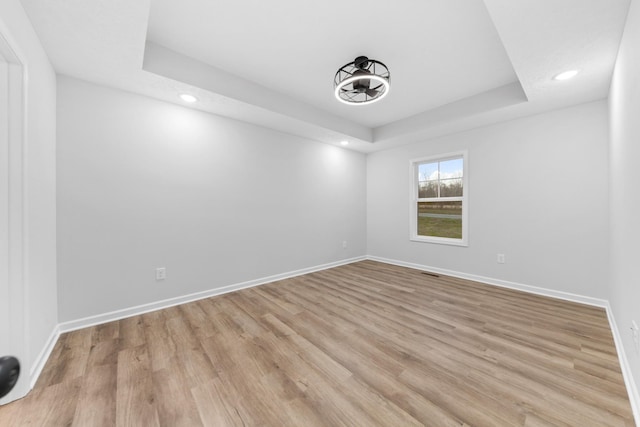 empty room featuring a tray ceiling, light wood-type flooring, recessed lighting, and baseboards