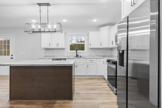 kitchen featuring decorative light fixtures, appliances with stainless steel finishes, light wood-style floors, white cabinets, and a kitchen island