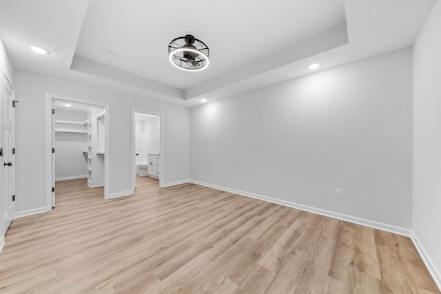 unfurnished bedroom with baseboards, a raised ceiling, a walk in closet, light wood-type flooring, and recessed lighting