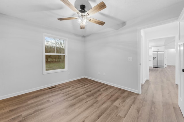 spare room featuring light wood finished floors, visible vents, baseboards, and ceiling fan