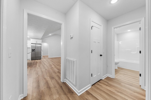 corridor featuring light wood finished floors, baseboards, and visible vents