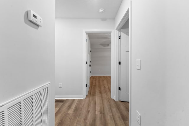 hall with baseboards, visible vents, and wood finished floors