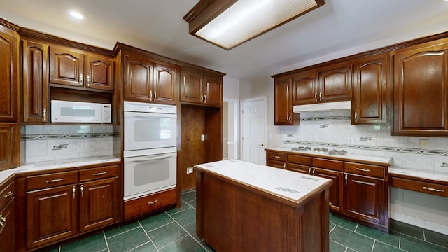 kitchen with dark tile patterned floors, white appliances, a center island, and backsplash