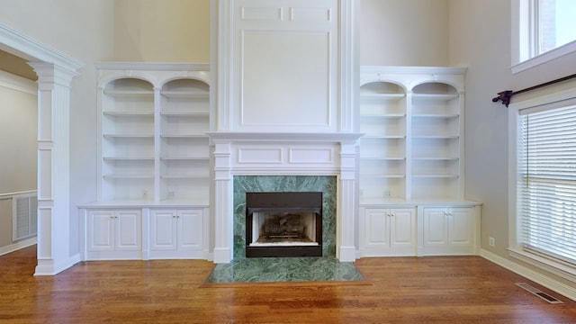 unfurnished living room featuring wood-type flooring, a fireplace, and built in shelves