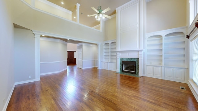 unfurnished living room featuring built in shelves, ceiling fan, a high end fireplace, wood-type flooring, and a high ceiling