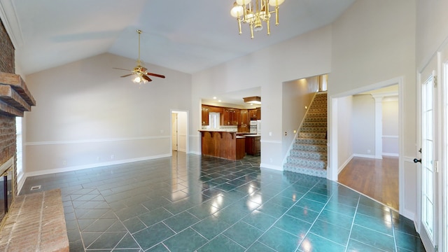 unfurnished living room featuring high vaulted ceiling, dark tile patterned flooring, ceiling fan with notable chandelier, and a fireplace