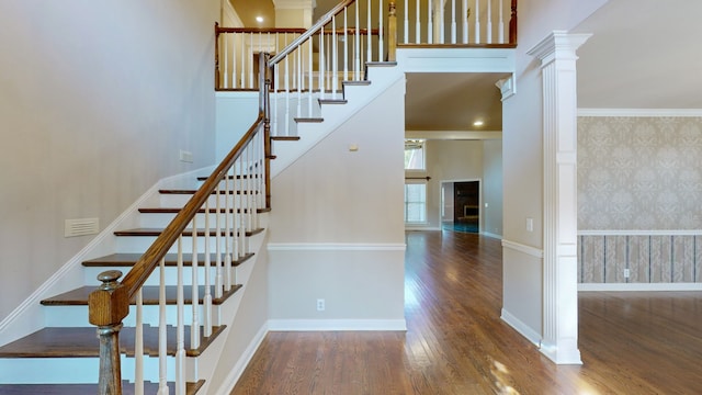 stairway featuring wood-type flooring, ornamental molding, and decorative columns