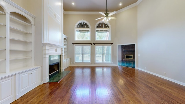 unfurnished living room with dark hardwood / wood-style flooring, a towering ceiling, crown molding, ceiling fan, and built in features