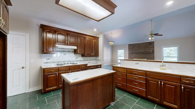 kitchen featuring ceiling fan, dark tile patterned flooring, sink, a center island, and decorative backsplash