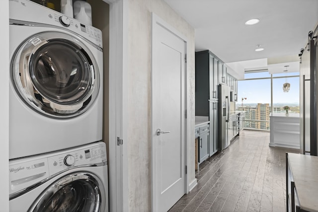 clothes washing area with stacked washer and clothes dryer, a barn door, and dark hardwood / wood-style floors