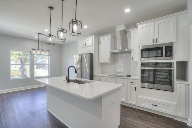 kitchen with wall chimney exhaust hood, decorative light fixtures, a center island with sink, stainless steel appliances, and white cabinets