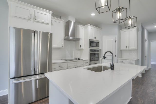 kitchen featuring wall chimney range hood, a kitchen island with sink, stainless steel appliances, hanging light fixtures, and white cabinets