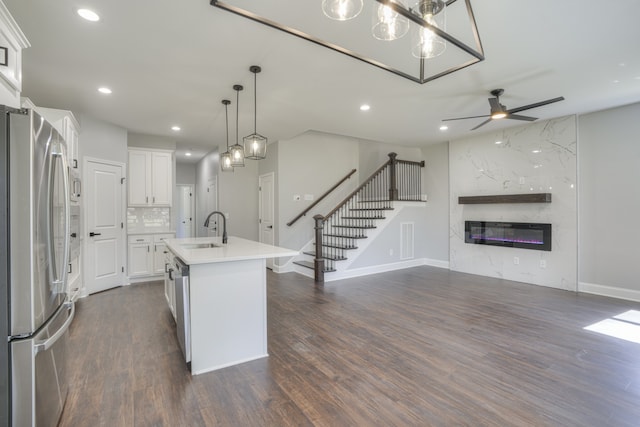 kitchen with a kitchen island with sink, sink, hanging light fixtures, appliances with stainless steel finishes, and white cabinetry