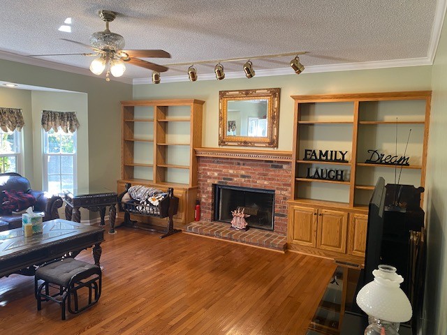 living room with a textured ceiling, wood-type flooring, ornamental molding, and a brick fireplace