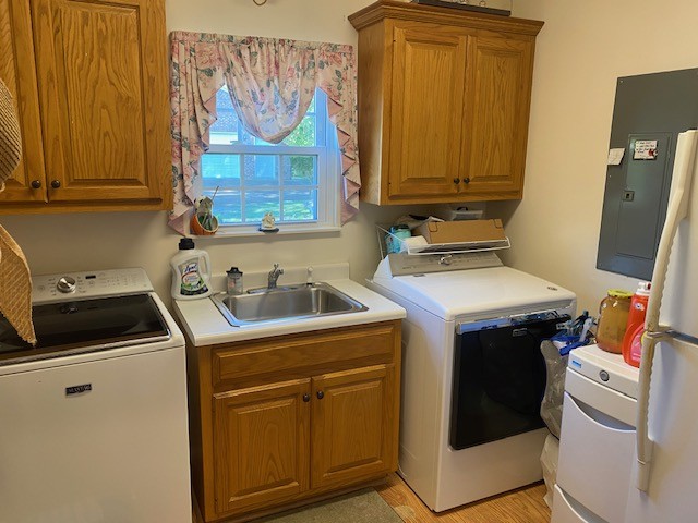 clothes washing area featuring washer and clothes dryer, electric panel, light hardwood / wood-style flooring, and sink