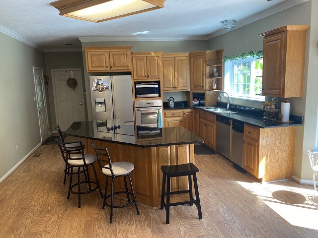 kitchen with light hardwood / wood-style floors, a breakfast bar area, sink, stainless steel appliances, and ornamental molding