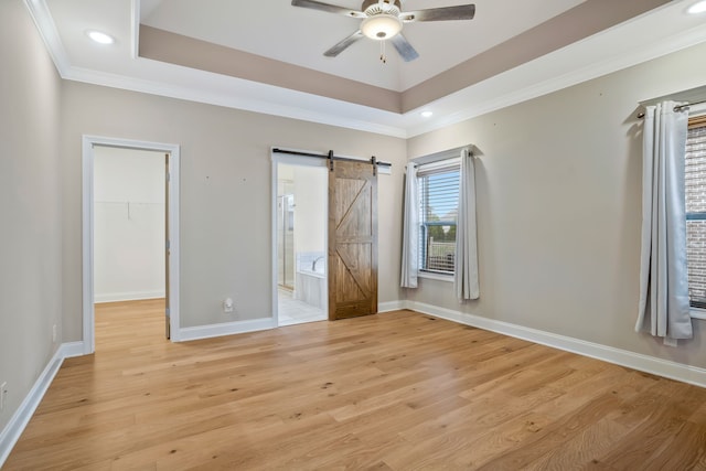 unfurnished bedroom featuring a spacious closet, light wood-type flooring, ceiling fan, and a barn door