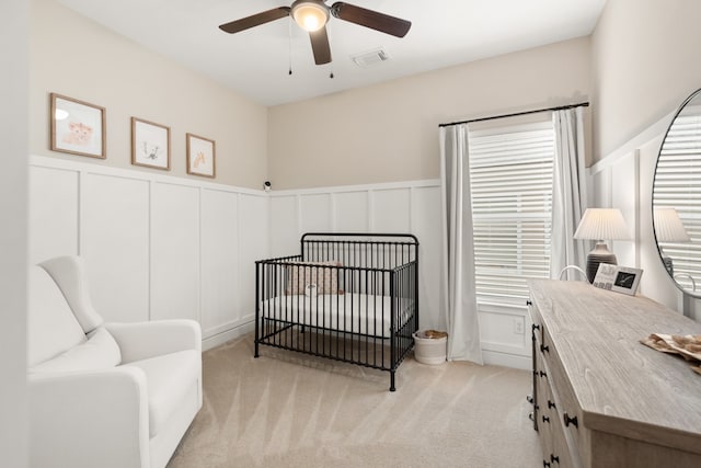 bedroom featuring a crib, light carpet, and ceiling fan