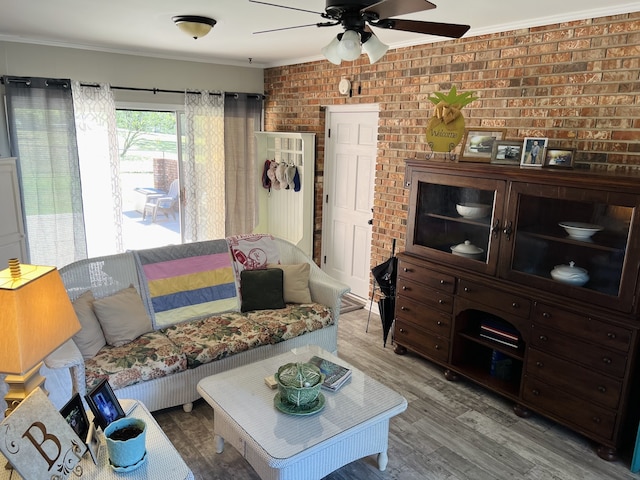 living room featuring brick wall, hardwood / wood-style flooring, crown molding, and ceiling fan