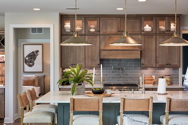 kitchen with dark brown cabinets, an island with sink, pendant lighting, and backsplash